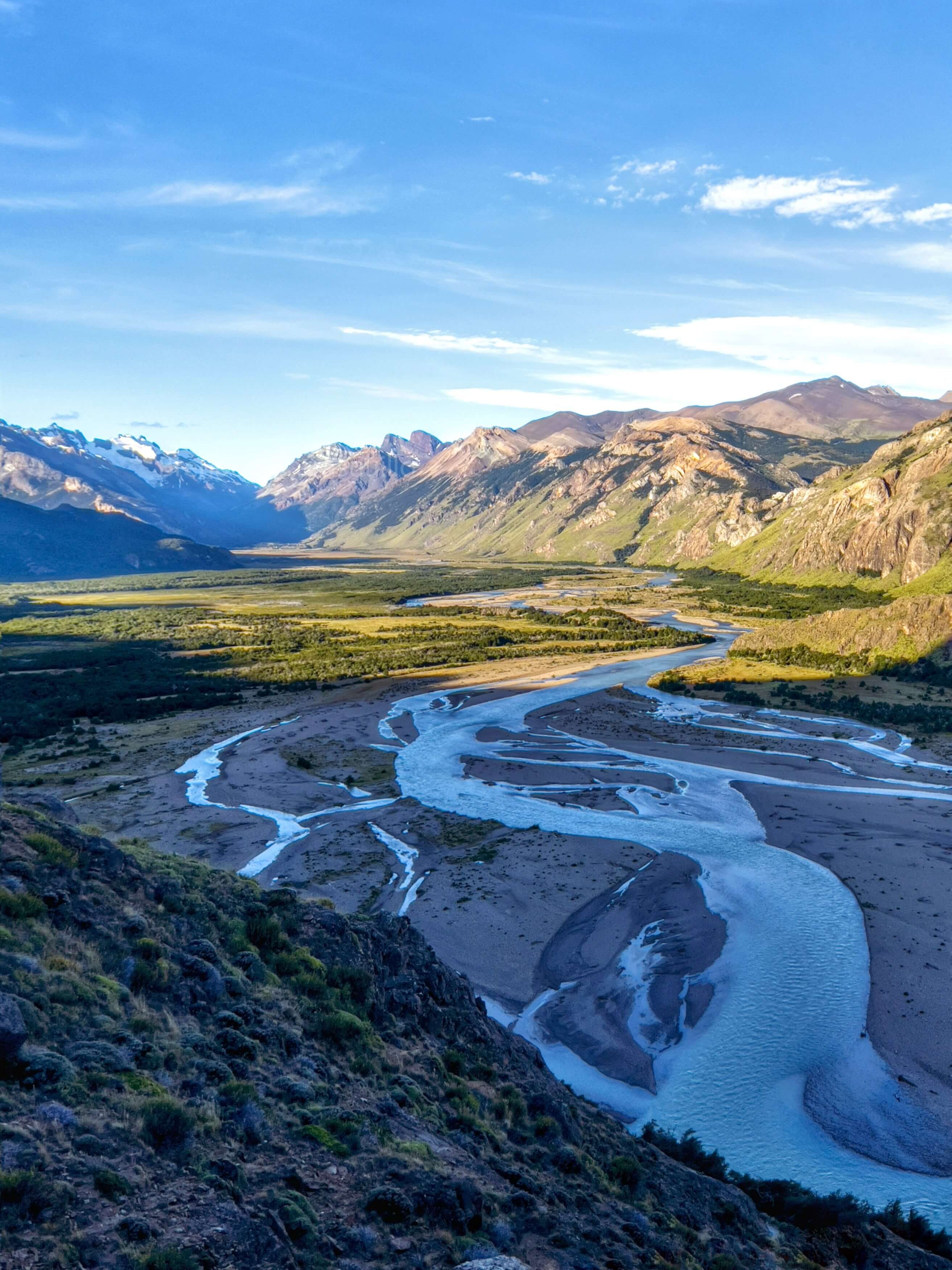 Winding river meandering through golden valley between mountain ranges