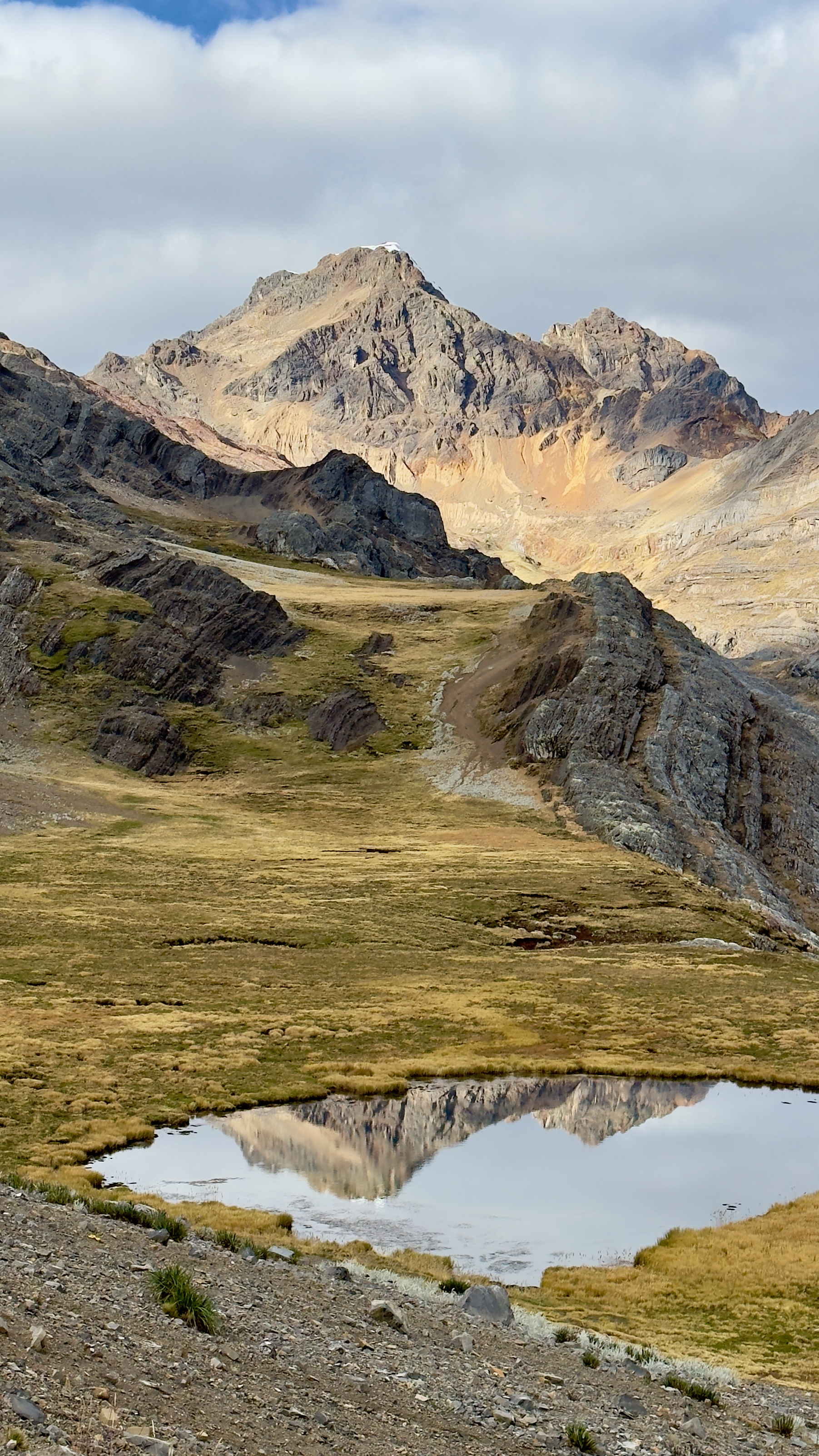 Small alpine tarn mirroring a jagged rocky peak in the high Peruvian Andes