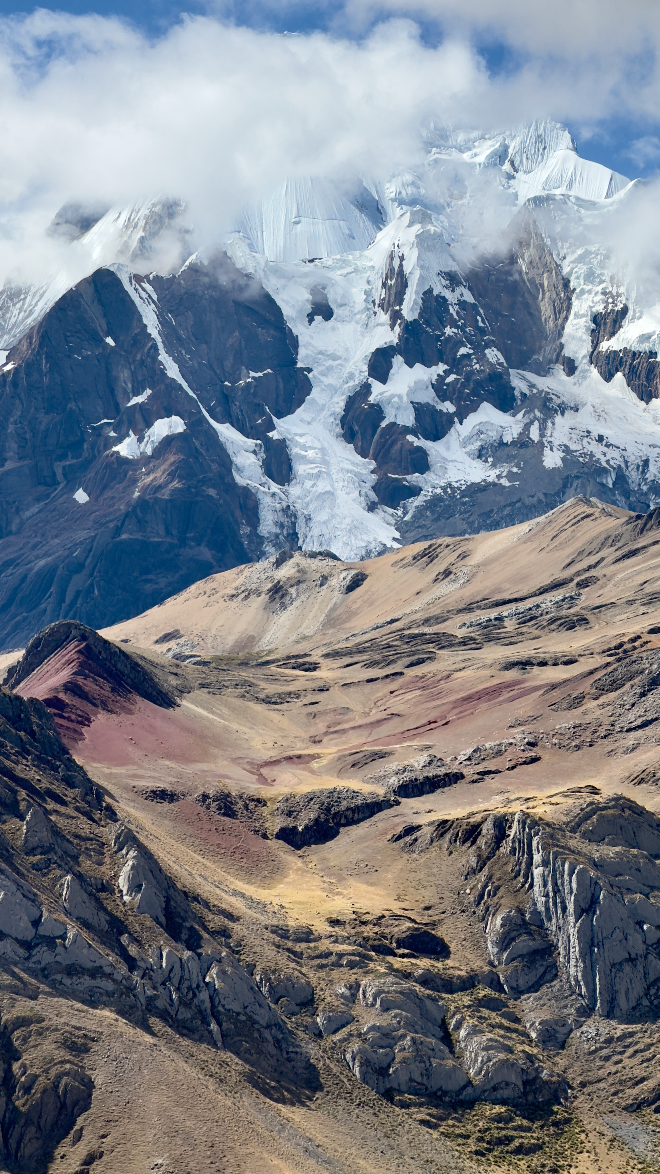 Heavily glaciated Andean peak rising above red-brown moraine slopes in the Cordillera Huayhuash
