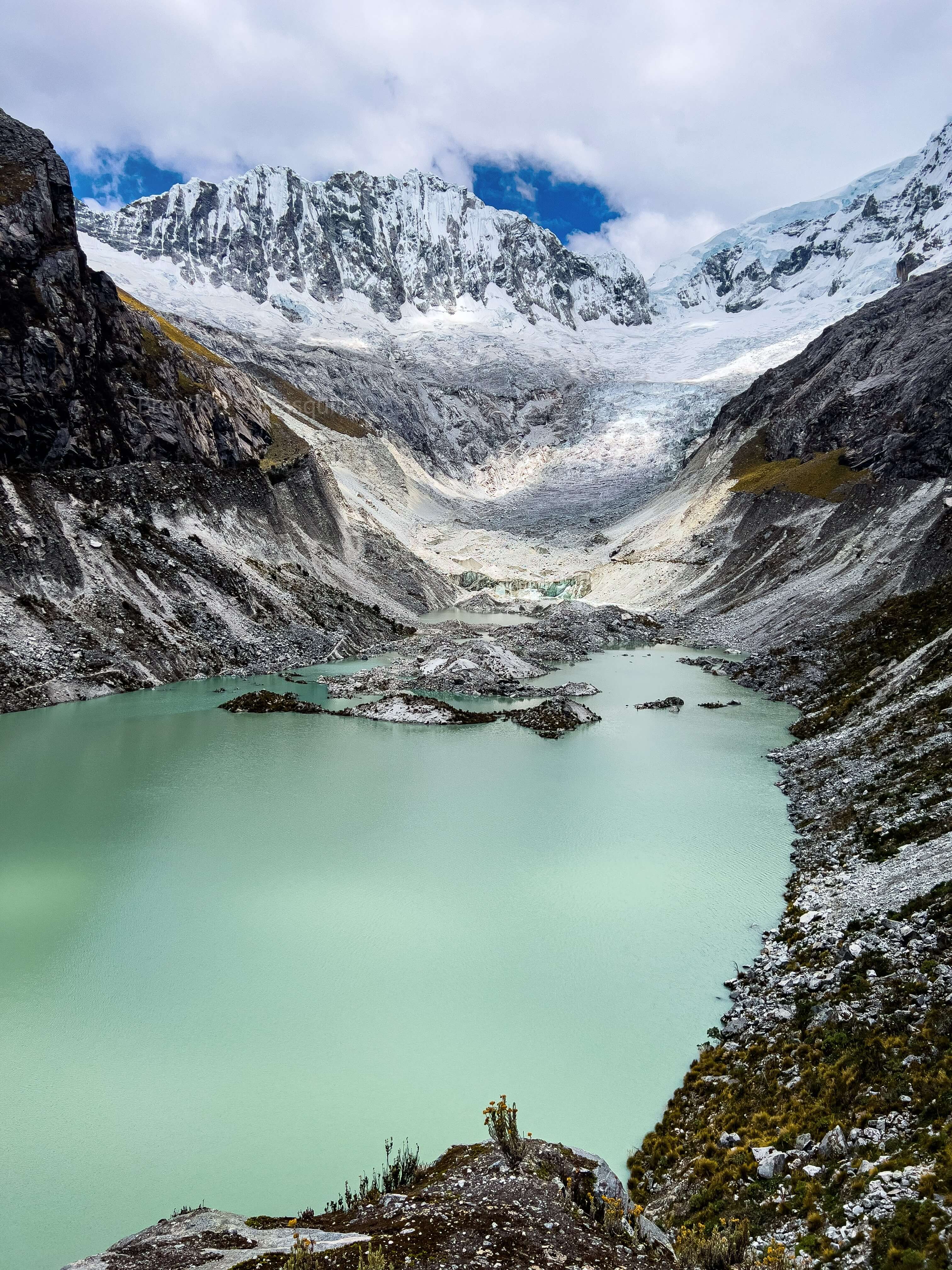 Turquoise glacial lake with snow-covered mountains and small figure visible