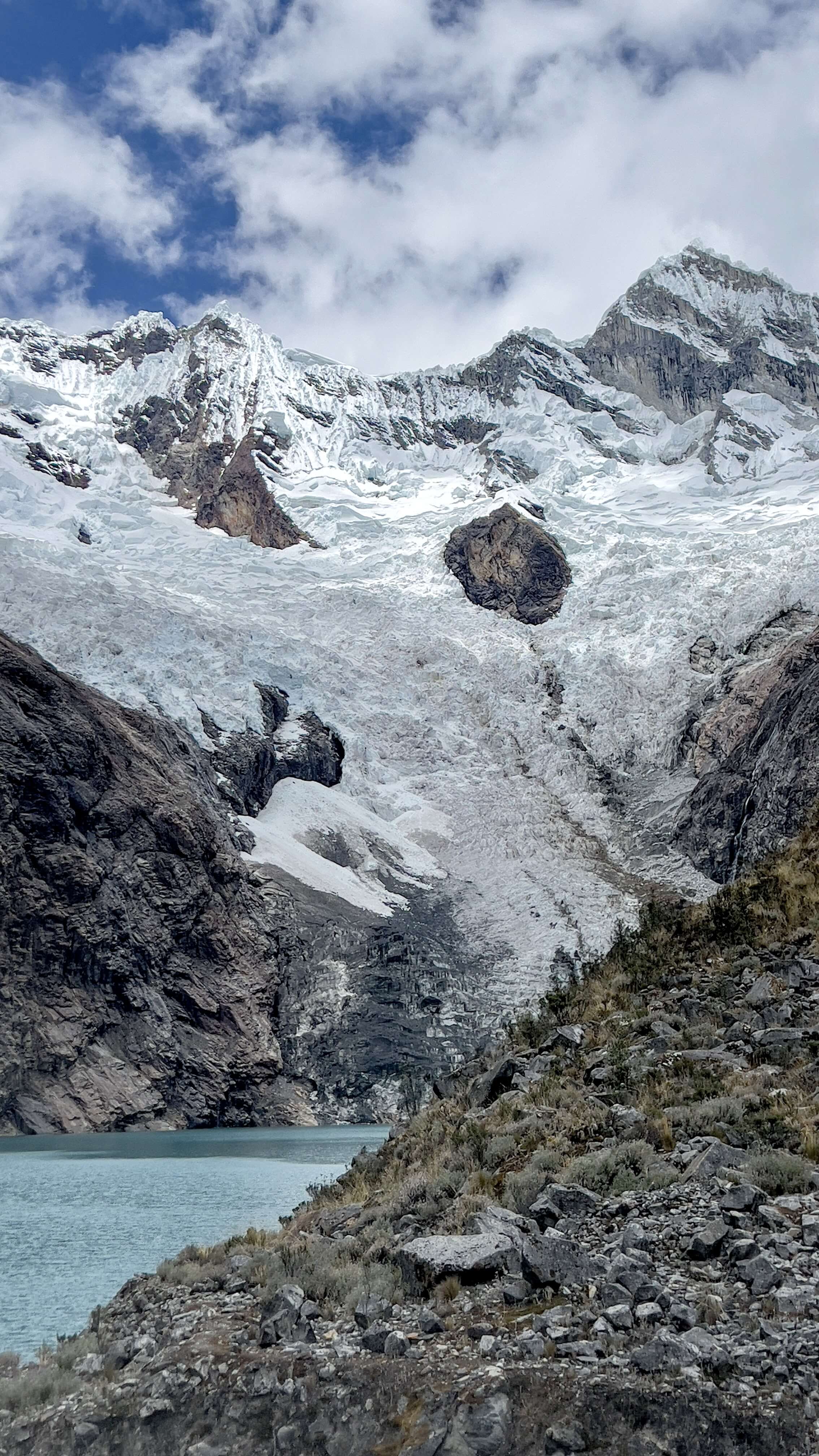 Glacial lake with hanging glacier and snow-covered peaks reflected in water