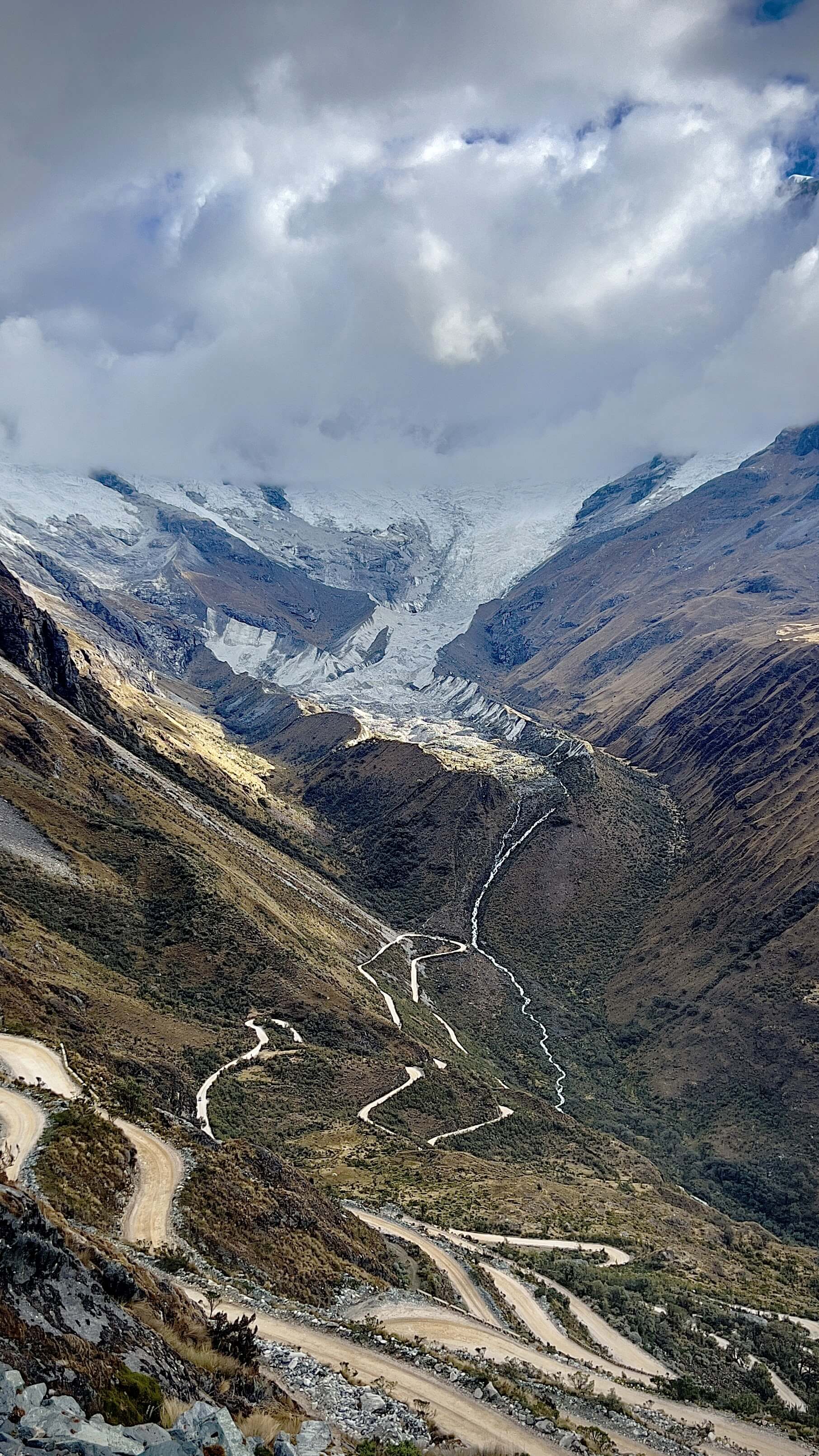 Winding mountain road descending through high-altitude Andean landscape with glacier views