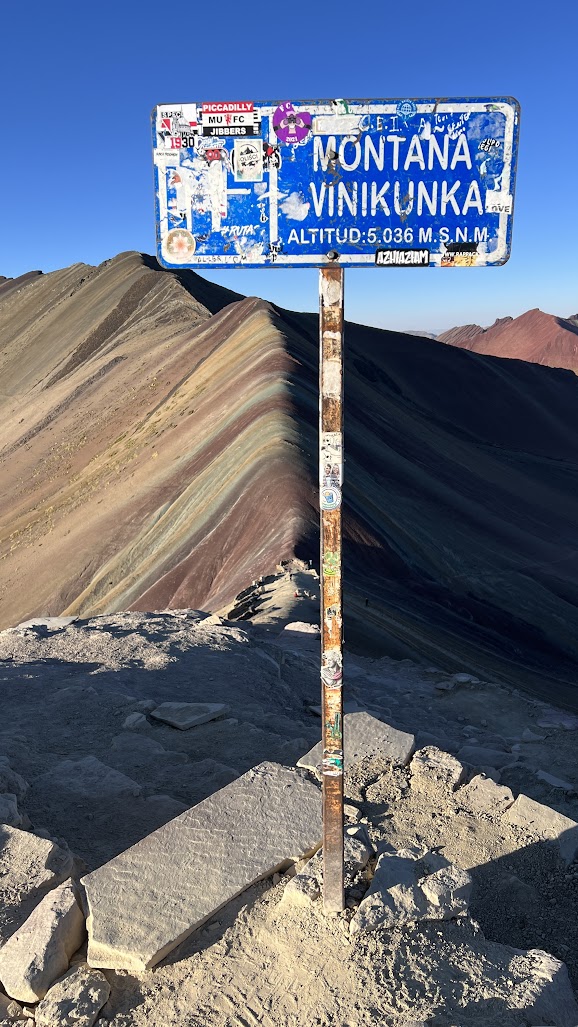 Colorful mineral-streaked mountain sign reading Montana Vinicunka at high altitude